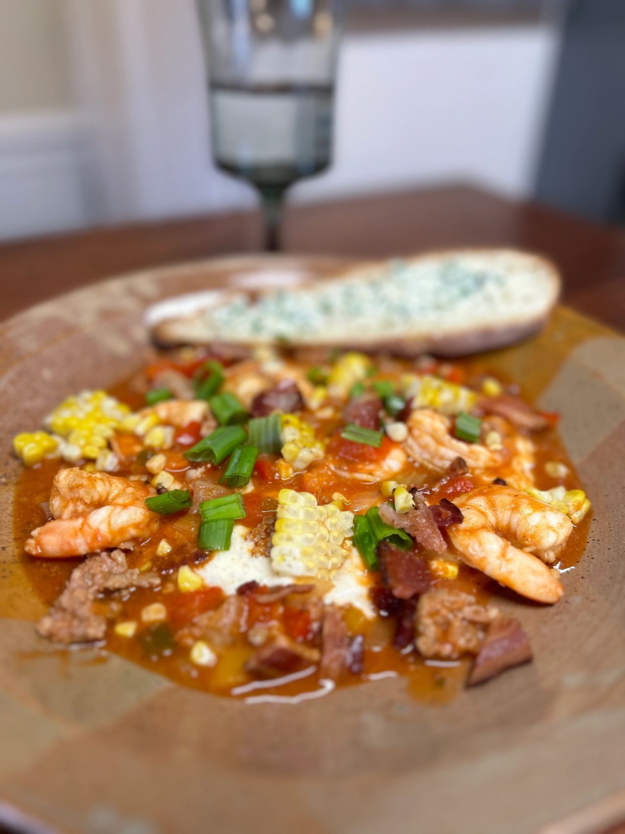 Shrimp and grits in a pottery bowl with bread in the background.