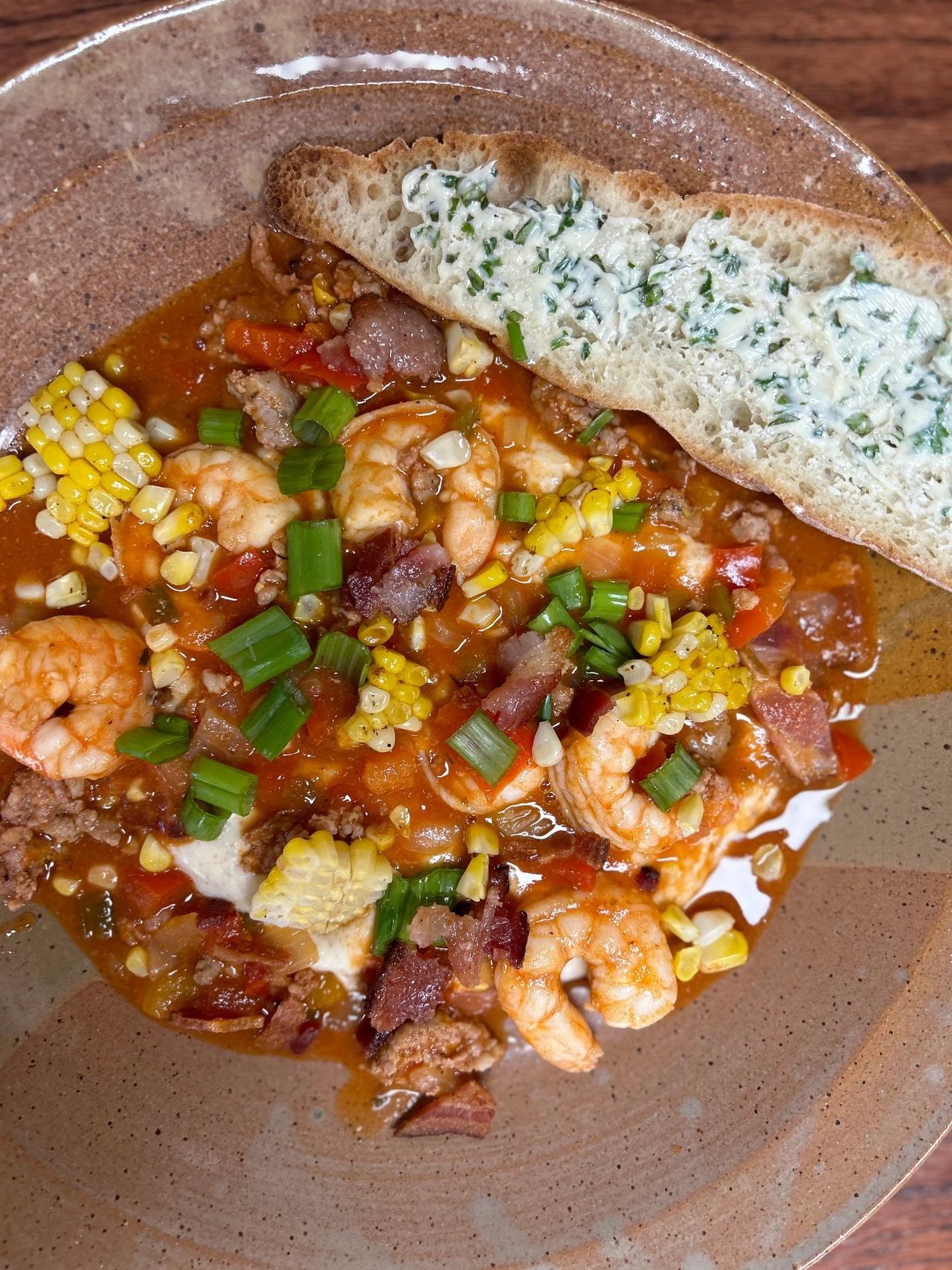 Shrimp and grits in pottery bowl with piece of buttered bread