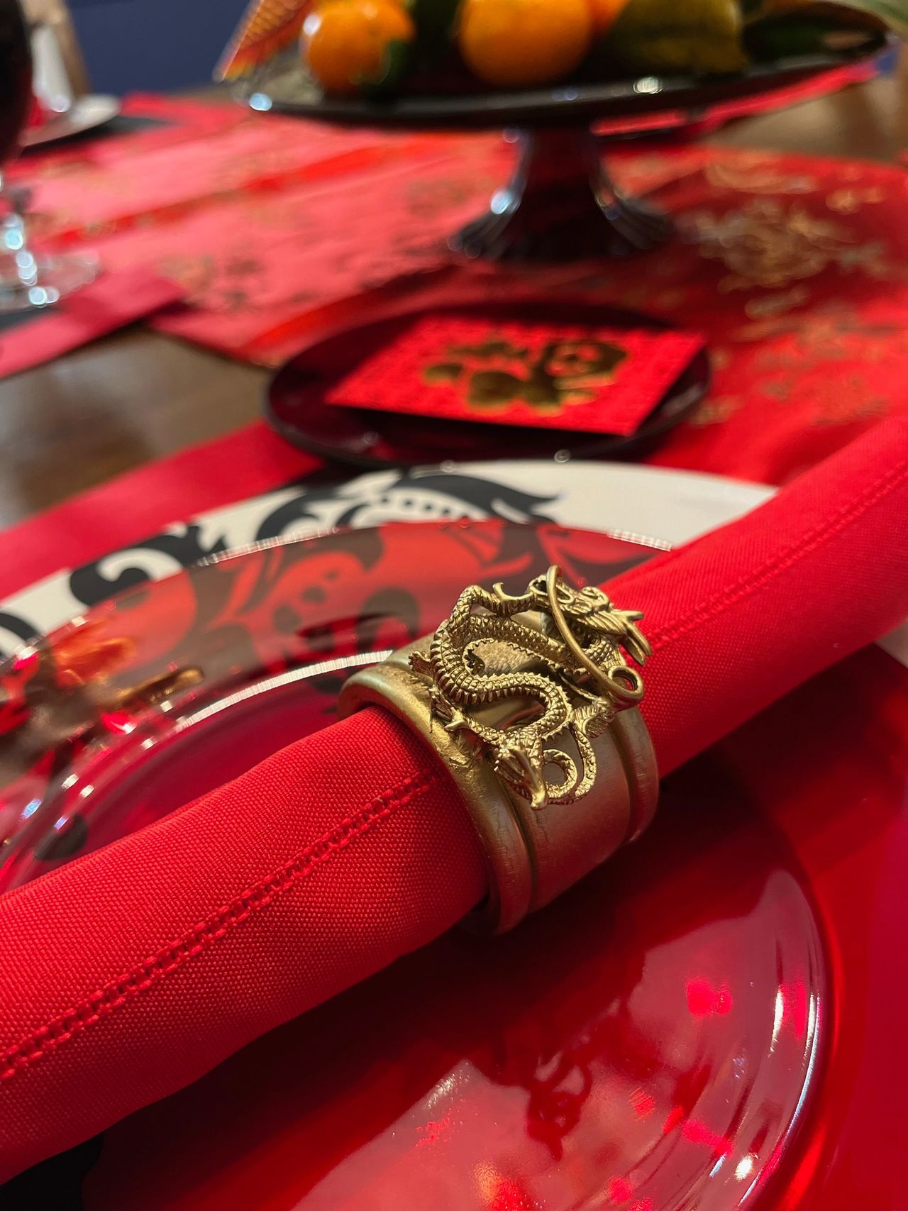 Gold Chinese dragon napkin ring, red napkin, red plate and Chinese fabric in background.