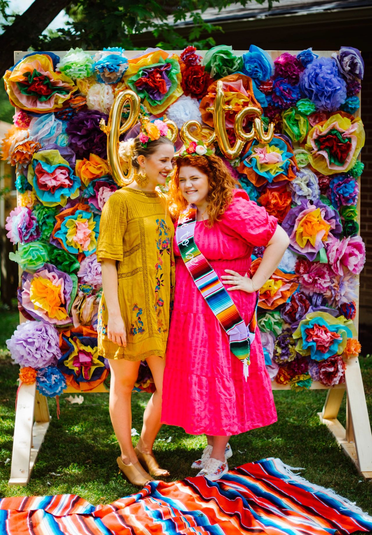 Two women dressed in bright colors in front of a fiesta photo backdrop.