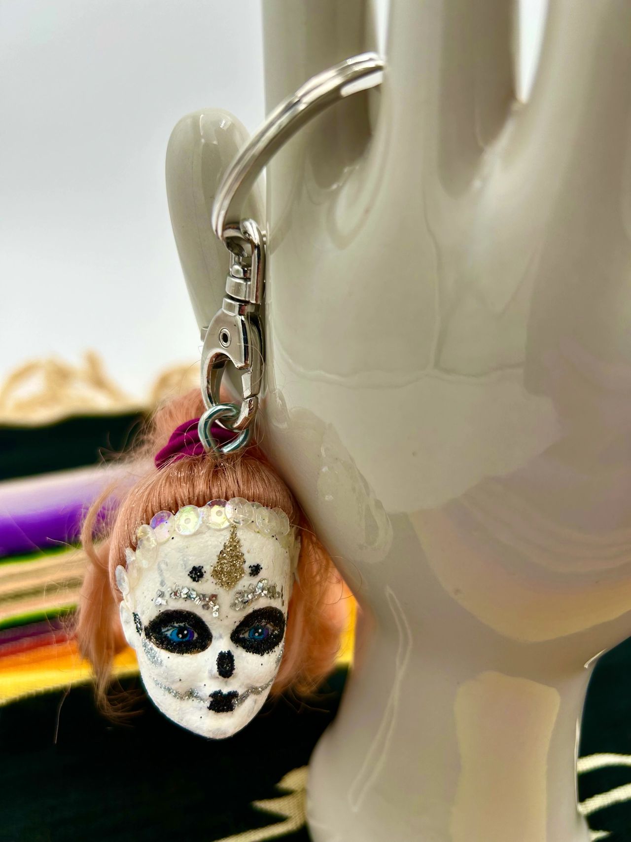 A painted Barbie head key chain hanging off a porcelain hand.