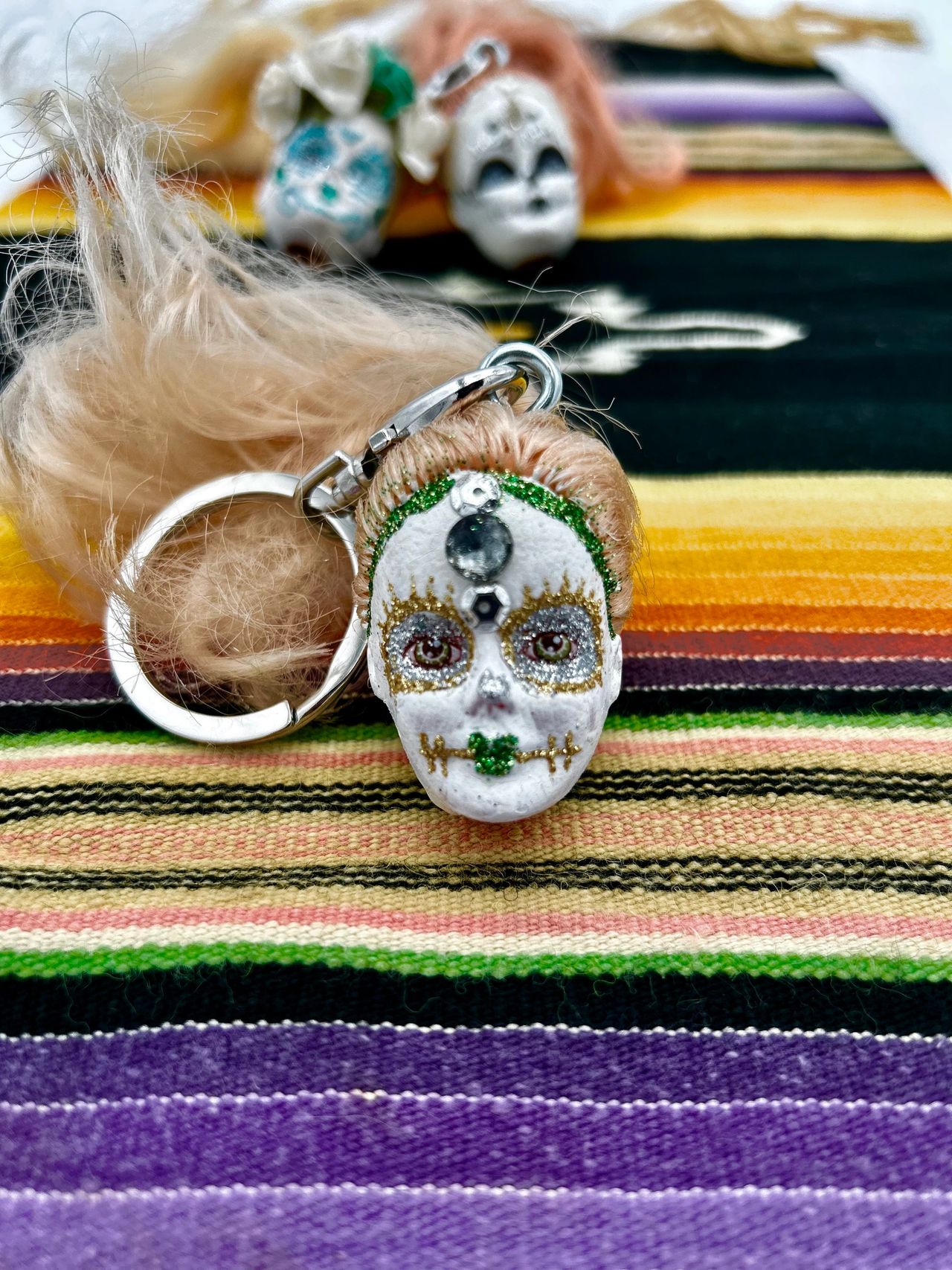 Decorated Barbie head key chain on Mexican blanket with 2 Barbie heads in the background.