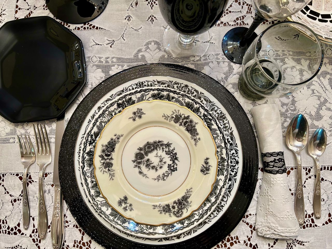 Layers of vintage dishes on a vintage lace tablecloth for an elegant Halloween tablescape.