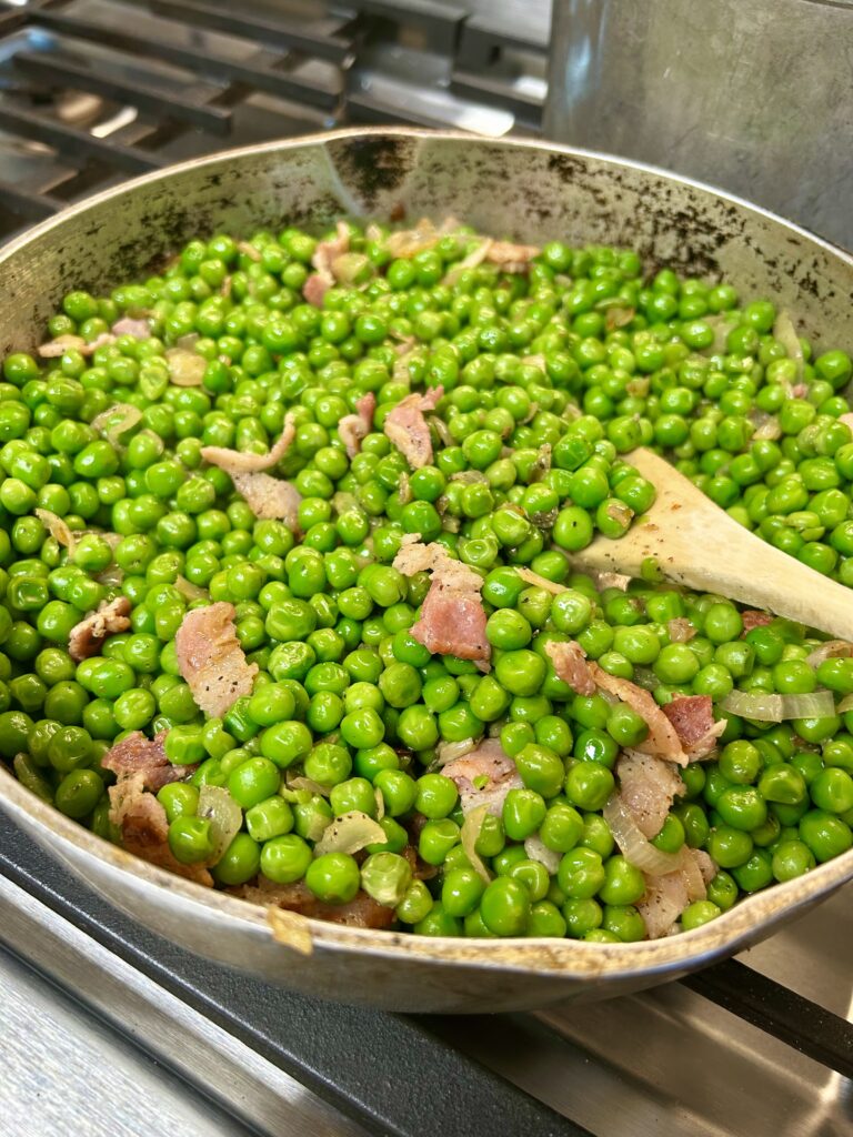 Green peas sautéed in a pan with bacon and black pepper